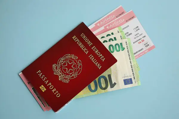 Italian passport with money and airline tickets on blue background close up. Tourism and travel concept