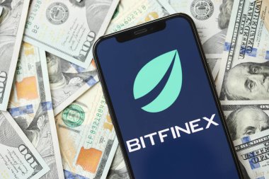 KYIV, UKRAINE - 15 Mart 2024 Btfinex logosu iPhone ekranında yüzlerce dolarlık banknotlarla. Kripto döviz portalı