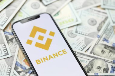 KYIV, UKRAINE - 15 Mart 2024 Binance logosu iPhone ekranında yüzlerce dolarlık banknotlarla. Kripto döviz portalı