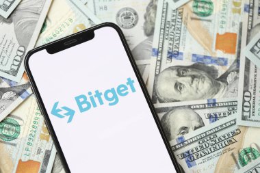 KYIV, UKRAINE - 15 Mart 2024 Bitget logosu iPhone ekranında yüzlerce dolarlık banknotlarla. Kripto döviz portalı