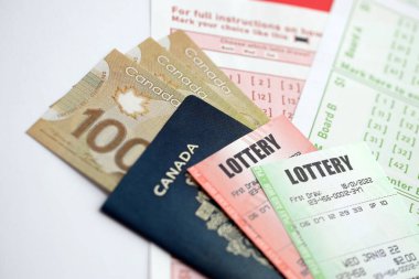 Piyango biletleri, kumar kağıtlarının üzerinde Kanada dolarlarıyla birlikte piyango oynamak için işaretlenmiş rakamlarla yatar. Piyango konsepti ya da kumar bağımlılığı