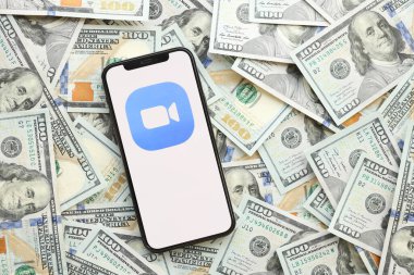 KYIV, UKRAINE - Nisan 1, 2024 Zoom simgesi akıllı telefon ekranında ve birçok kullanışlı para kaynağı. Uygulama logolu iPhone görüntüsü ve bir sürü yüz dolarlık banknotlar