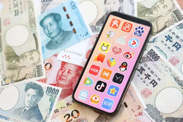 stock image KYIV, UKRAINE - APRIL 1, 2024 Asian apps icon on smartphone screen on many asian money bills. iPhone display with app logo with japanese yen and chinese yuan banknotes