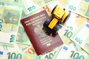 Red polish passport and yellow tractor on euro money bills close up clipart