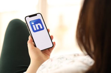 KYIV, UKRAINE - Nisan 1, 2024 LinkedIn simgesi akıllı telefon ekranında kapalı alanda genç kadınların elinde. iPhone uygulaması kullanan kadın