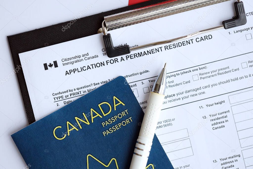 Application for permanent resident card on table with pen and canadian passport close up