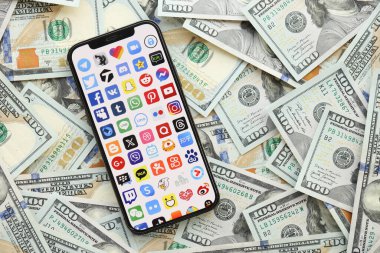 KYIV, UKRAINE - Nisan 1, 2024 Akıllı telefon ekranında birçok uygulama simgesi ve birçok kullanım parası. Uygulama logolu iPhone görüntüsü ve bir sürü yüz dolarlık banknotlar
