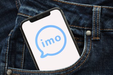 KYIV, UKRAINE - 1 Nisan 2024 İmo kurye simgesi kot pantolon cebinde akıllı telefon ekranında. Uygulama logosuna sahip iPhone görüntüsü. Moda görünümlü kotların cebinde gizleniyor.