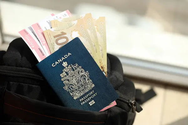 Canadian passport and dollar money bills with airline tickets on backpack close up