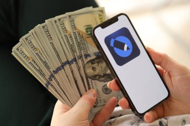 KYIV, UKRAINE - Nisan 1, 2024 Akıllı telefon ekranında LiveJournal simgesi ve kadın elinde para. Uygulama logolu iPhone görüntüsü ve kızların elinde 100 dolarlık banknotlar