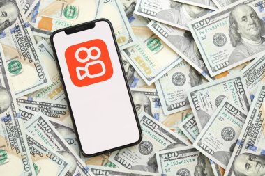 KYIV, UKRAINE - Nisan 1, 2024 Kuaishou platform simgesi akıllı telefon ekranında ve birçok kullanım parası faturası. Uygulama logolu iPhone görüntüsü ve bir sürü yüz dolarlık banknotlar