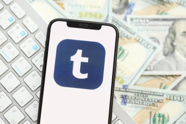KYIV, UKRAINE - Nisan 1, 2024 Tumblr simgesi birçok kullanışlı para banknotlarında akıllı telefon ekranında. Uygulama logosuna sahip iPhone görüntüsü ve beyaz klavyeli dolar banknotları