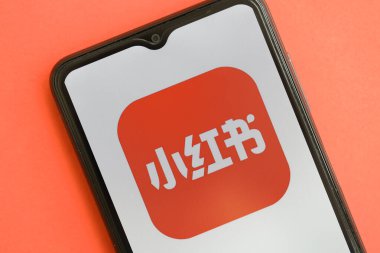 KYIV, UKRAINE - 1 Nisan 2024 Xiaohongshu simgesi kırmızı masadaki akıllı telefon ekranında. Parlak kırmızı arkaplanda uygulama logosuna sahip iPhone görüntüsü
