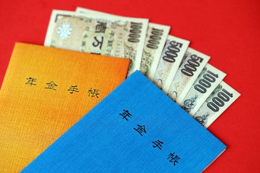 Japon emeklilik sigortası broşürleri yen para faturalarıyla dolu masada. Japon emekliler için mavi ve turuncu kitaplar kapanıyor.