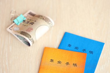 Japon emeklilik sigortası broşürleri yen para faturalarıyla dolu masada. Japon emekliler için mavi ve turuncu kitaplar kapanıyor.