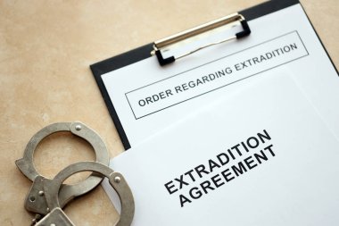 Extradition Agreement and Order Regarding Extradition with handcuffs on table close up clipart