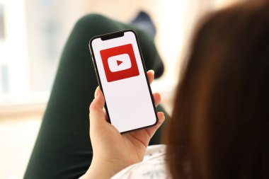 KYIV, UKRAINE - Nisan 1, 2024 Youtube simgesi akıllı telefon ekranında kapalı alanda genç kadınların elinde. iPhone uygulaması kullanan kadın