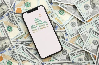 KYIV, UKRAINE - 1 Nisan 2024 Oasis simgesi akıllı telefon ekranında ve birçok kullanım dışı para banknotları. Uygulama logolu iPhone görüntüsü ve bir sürü yüz dolarlık banknotlar