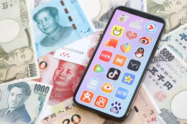 stock image KYIV, UKRAINE - APRIL 1, 2024 Asian apps icon on smartphone screen on many asian money bills. iPhone display with app logo with japanese yen and chinese yuan banknotes