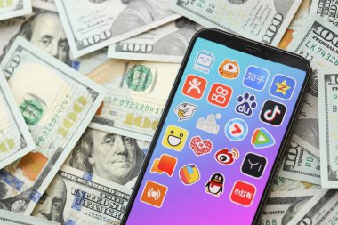 KYIV, UKRAINE - Nisan 1, 2024 Asya uygulamaları simgesi akıllı telefon ekranında ve birçok kullanım parası faturası. Uygulama logolu iPhone görüntüsü ve bir sürü yüz dolarlık banknotlar