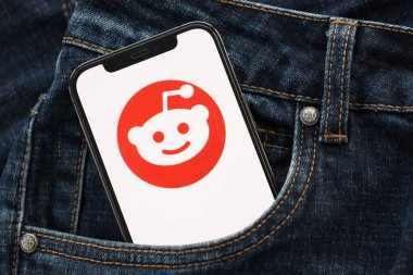 KYIV, UKRAINE - 1 Nisan 2024 Reddit simgesi kot pantolon cebinde akıllı telefon ekranında. Uygulama logosuna sahip iPhone görüntüsü. Moda görünümlü kotların cebinde gizleniyor.