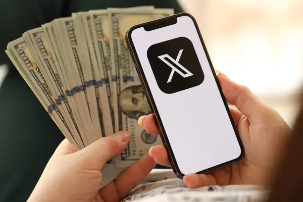 stock image KYIV, UKRAINE - APRIL 1, 2024 Twitter X icon on smartphone screen and money in female hand. iPhone display with app logo and hundred dollar bills in girls hands close up