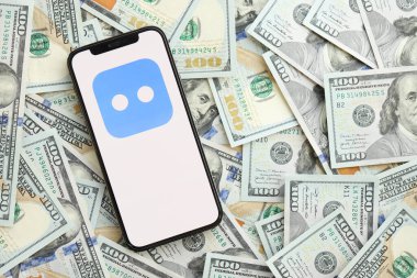KYIV, UKRAINE - 1 Nisan 2024 Botim kurye simgesi akıllı telefon ekranında ve birçok kullanım dışı para banknotları. Uygulama logolu iPhone görüntüsü ve bir sürü yüz dolarlık banknotlar