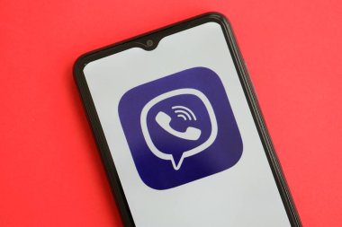 KYIV, UKRAINE - 1 Nisan 2024 Viber kurye simgesi kırmızı masadaki akıllı telefon ekranında. Parlak kırmızı arkaplanda uygulama logosuna sahip iPhone görüntüsü