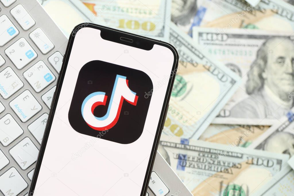 KYIV, UKRAINE - APRIL 1, 2024 TikTok or Douyin icon on smartphone screen on many usd money bills. iPhone display with app logo and dollar banknotes with white keyboard