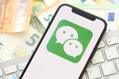 KYIV, UKRAINE - 1 Nisan 2024 Wechat veya Weixin simgesi birçok avro para banknotlarında akıllı telefon ekranında. Avrupa para birimi avro banknotları ve beyaz klavyeli uygulamalı iPhone görüntüsü