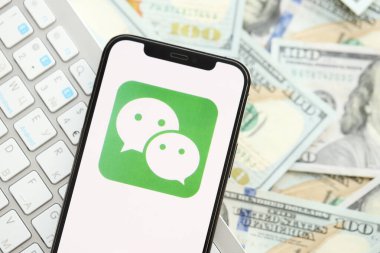 KYIV, UKRAINE - Nisan 1, 2024 Wechat veya Weixin simgesi birçok kullanım dışı para banknotlarında akıllı telefon ekranında. Uygulama logosuna sahip iPhone görüntüsü ve beyaz klavyeli dolar banknotları