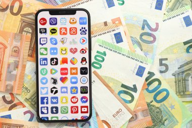 KYIV, UKRAINE - Nisan 1, 2024 Birçok akıllı telefon ekranındaki birçok uygulama simgesi Avro para banknotlarında. Avrupa para birimi euro banknotlu uygulama logosuyla iPhone görüntüsü