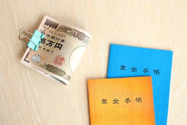 Japon emeklilik sigortası broşürleri yen para faturalarıyla dolu masada. Japon emekliler için mavi ve turuncu kitaplar kapanıyor.