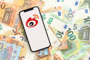 KYIV, UKRAINE - Nisan 1, 2024 Sina Weibo simgesi birçok avro banknotunda akıllı telefon ekranında. Avrupa para birimi euro banknotlu uygulama logosuyla iPhone görüntüsü