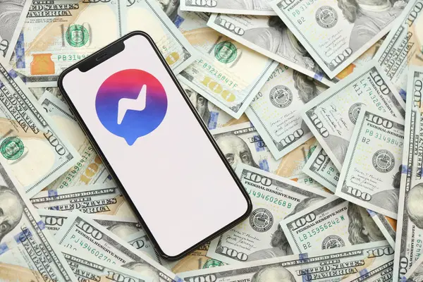 KYIV, UKRAINE - 1 Nisan 2024 Facebook Messenger simgesi, akıllı telefon ekranı ve birçok kullanıcı parası. Uygulama logolu iPhone görüntüsü ve bir sürü yüz dolarlık banknotlar