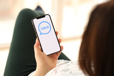 KYIV, UKRAINE - Nisan 1, 2024 İmo kurye simgesi akıllı telefon ekranında kapalı alandaki genç kadınların elinde. iPhone uygulaması kullanan kadın