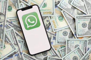 KYIV, UKRAINE - 1 Nisan 2024 Whatsapp kurye simgesi akıllı telefon ekranında ve birçok kullanım dışı para banknotları. Uygulama logolu iPhone görüntüsü ve bir sürü yüz dolarlık banknotlar