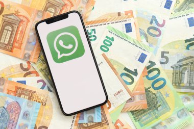 KYIV, UKRAINE - APRIL 1, 2024 Whatsapp messenger icon on smartphone screen on many euro money bills. iPhone display with app logo with european currency euro banknotes clipart