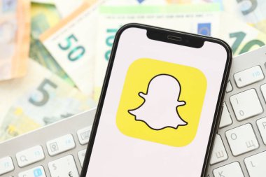 KYIV, UKRAINE - 1 Nisan 2024 Snapchat simgesi birçok avro para bankasında akıllı telefon ekranında. Avrupa para birimi avro banknotları ve beyaz klavyeli uygulamalı iPhone görüntüsü