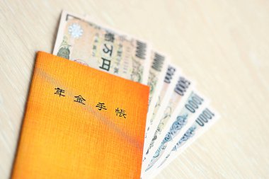 Yen para faturalarının olduğu masada Japon emeklilik sigortası var. Japon emekliler için turuncu kitap kapanıyor.