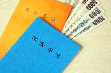Japon emeklilik sigortası broşürleri yen para faturalarıyla dolu masada. Japon emekliler için mavi ve turuncu kitaplar kapanıyor.