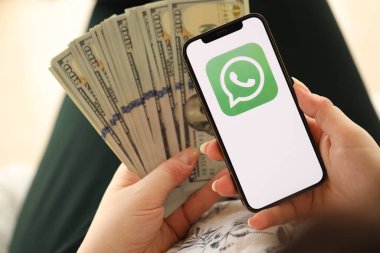 KYIV, UKRAINE - APRIL 1, 2024 Whatsapp messenger icon on smartphone screen and money in female hand. iPhone display with app logo and hundred dollar bills in girls hands close up clipart