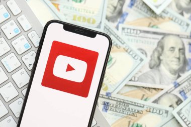 KYIV, UKRAINE - Nisan 1, 2024 Youtube simgesi birçok kullanışlı para banknotlarında akıllı telefon ekranında. Uygulama logosuna sahip iPhone görüntüsü ve beyaz klavyeli dolar banknotları