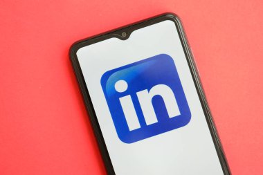 KYIV, UKRAINE - 1 Nisan 2024 LinkedIn simgesi kırmızı masadaki akıllı telefon ekranında. Parlak kırmızı arkaplanda uygulama logosuna sahip iPhone görüntüsü