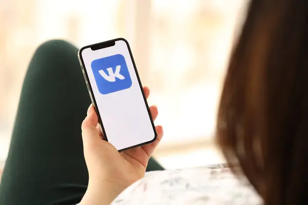 stock image KYIV, UKRAINE - APRIL 1, 2024 Vkontakte icon on smartphone screen in young female hands indoors. Woman using iPhone app at home
