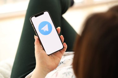 KYIV, UKRAINE - 1 Nisan 2024 Telegram kurye ikonu akıllı telefon ekranında kapalı alanda genç kadınların elinde. iPhone uygulaması kullanan kadın