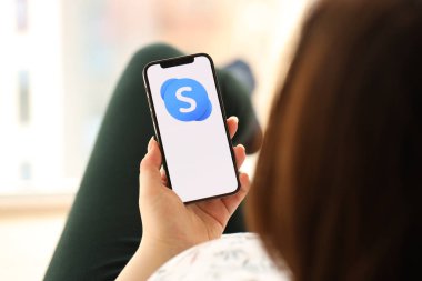 KYIV, UKRAINE - Nisan 1, 2024 Skype simgesi, akıllı telefon ekranında, kapalı alanda genç kadınların elinde. iPhone uygulaması kullanan kadın