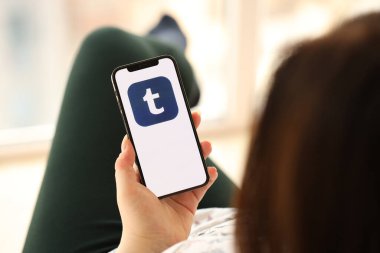 KYIV, UKRAINE - Nisan 1, 2024 Tumblr simgesi akıllı telefon ekranında kapalı alanda genç kadınların elinde. iPhone uygulaması kullanan kadın