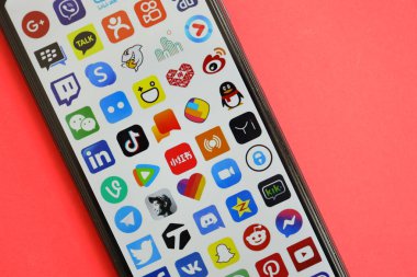 KYIV, UKRAINE - 1 Nisan 2024 Kırmızı masadaki akıllı telefon ekranında birçok uygulama simgesi. Parlak kırmızı arkaplanda uygulama logosuna sahip iPhone görüntüsü