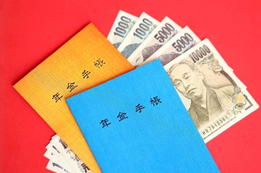 Japon emeklilik sigortası broşürleri yen para faturalarıyla dolu masada. Japon emekliler için mavi ve turuncu kitaplar kapanıyor.